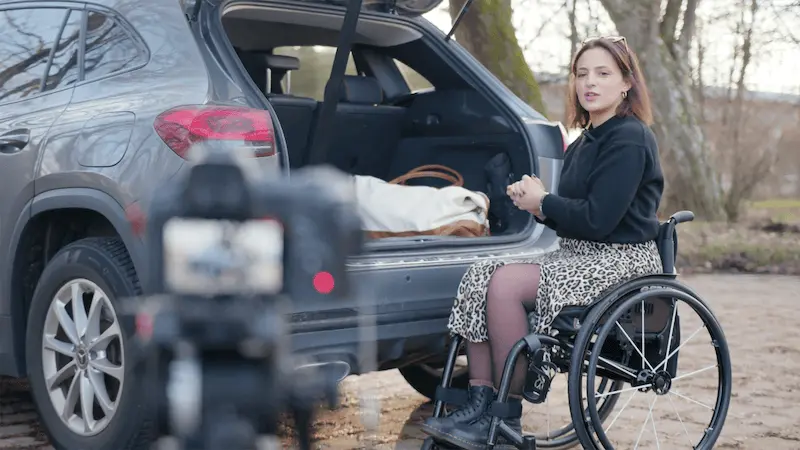 Rollstuhlfahrerin die etwas in den Kofferraum ihres Autos läd